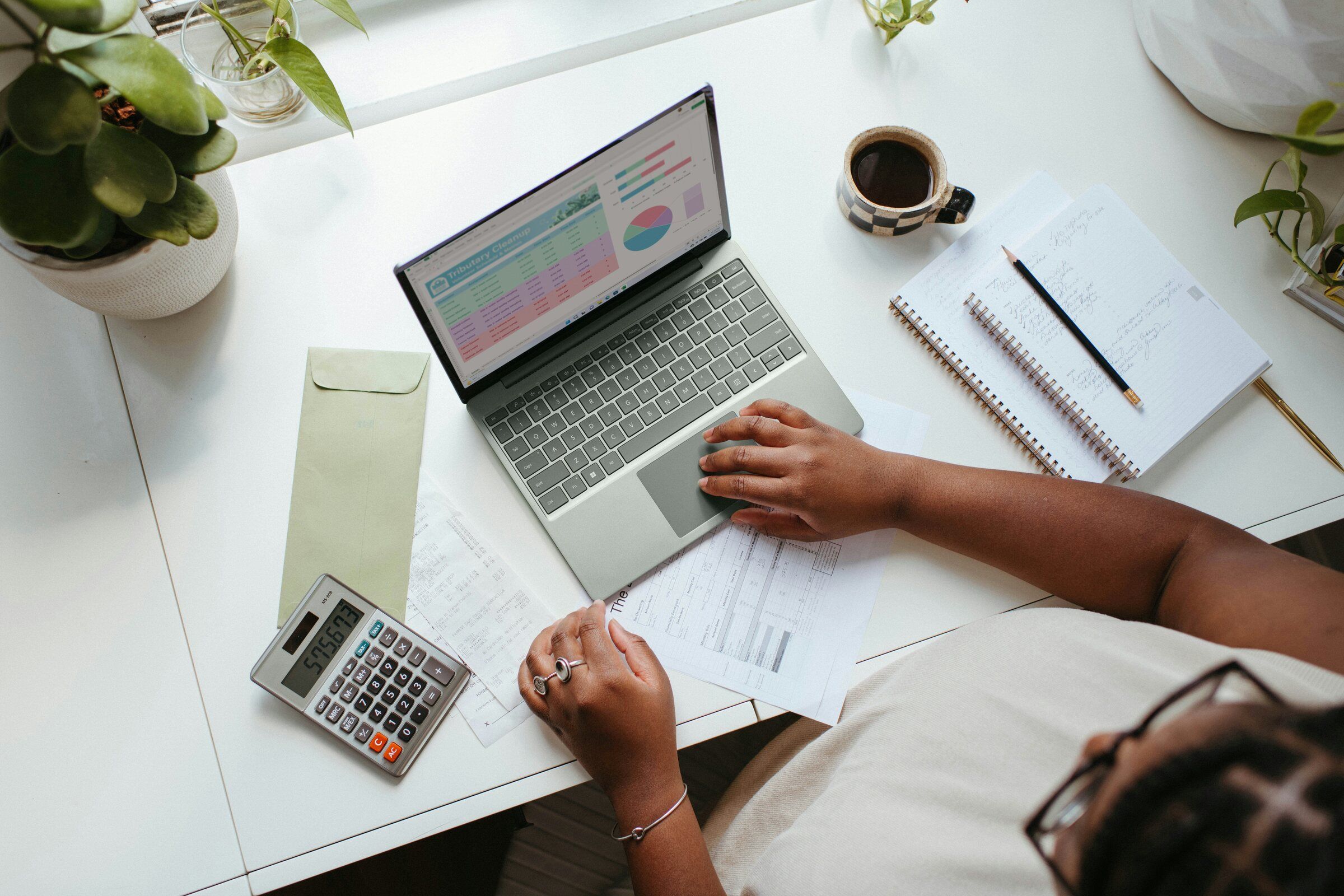 Someone working through payroll figures on a laptop with a calculator beside it