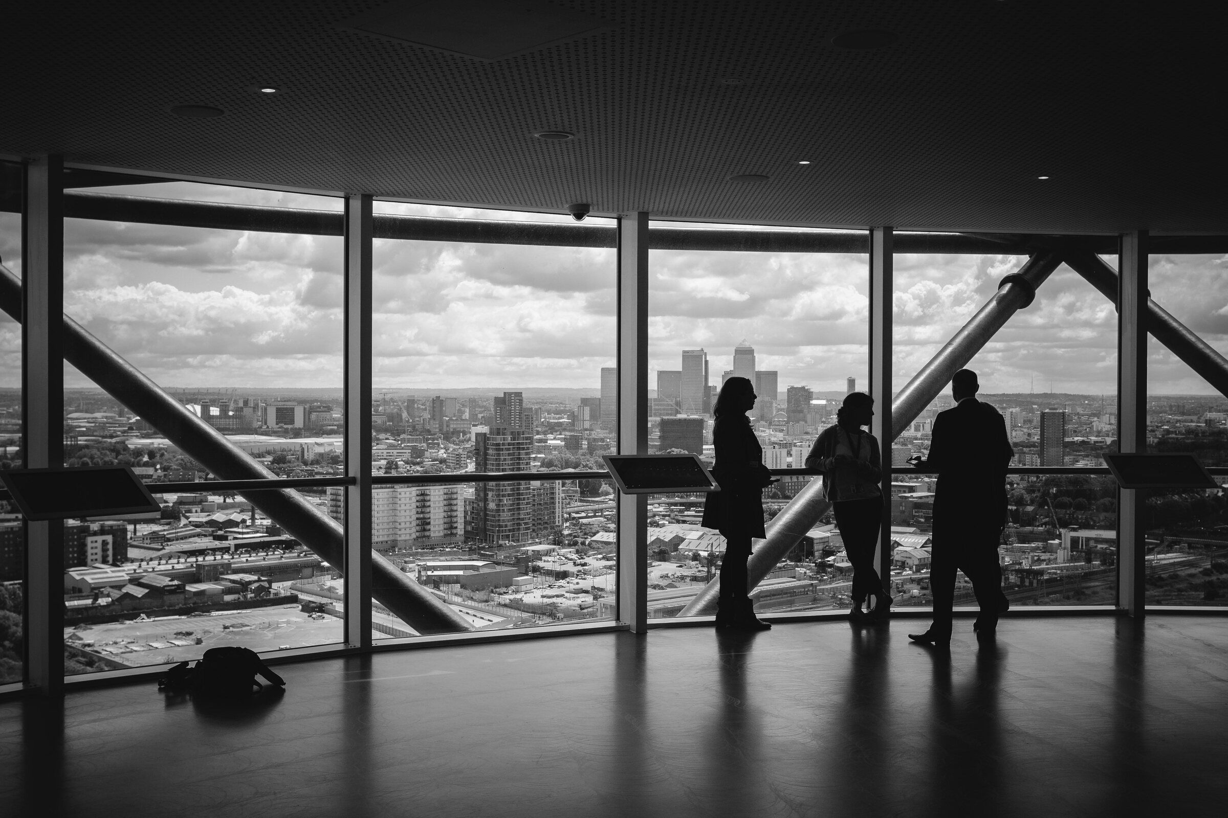 Three people looking out over a city through tall office windows